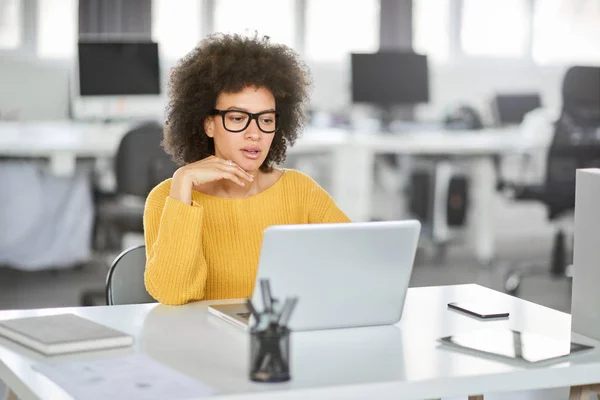 Sério mista mulher de negócios vestido casual sentado no escritório moderno e usando laptop . — Fotografia de Stock