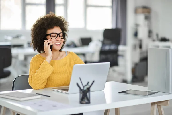 Charming mixt cursa femeie de afaceri îmbrăcat casual folosind telefon inteligent și laptop, în același timp, în timp ce stau în birou modern . — Fotografie, imagine de stoc