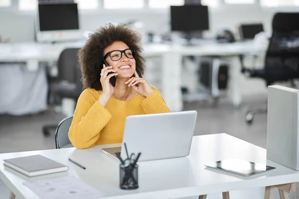 Fermecătoare rasă mixtă femeie de afaceri îmbrăcat casual folosind telefon inteligent în timp ce stau în birou modern . — Fotografie, imagine de stoc