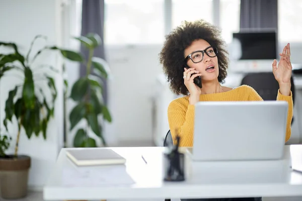Fermecătoare rasă mixtă femeie de afaceri îmbrăcat casual folosind telefon inteligent în timp ce stau în birou modern . — Fotografie, imagine de stoc