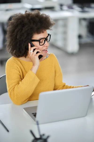 Hermosa mujer de negocios de raza mixta hablando en el teléfono inteligente y el uso de la tableta mientras está sentado en la oficina moderna . — Foto de Stock