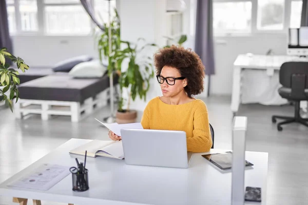 Ernsthafte gemischte Rasse attraktive Geschäftsfrau elegant lässig gekleidet hält Papierkram, während sie im modernen Büro sitzt. — Stockfoto