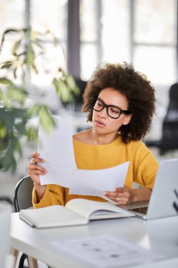 Modern ofiste otururken ciddi karışık ırk çekici iş kadını akıllı rahat holding evrak giyinmiş.