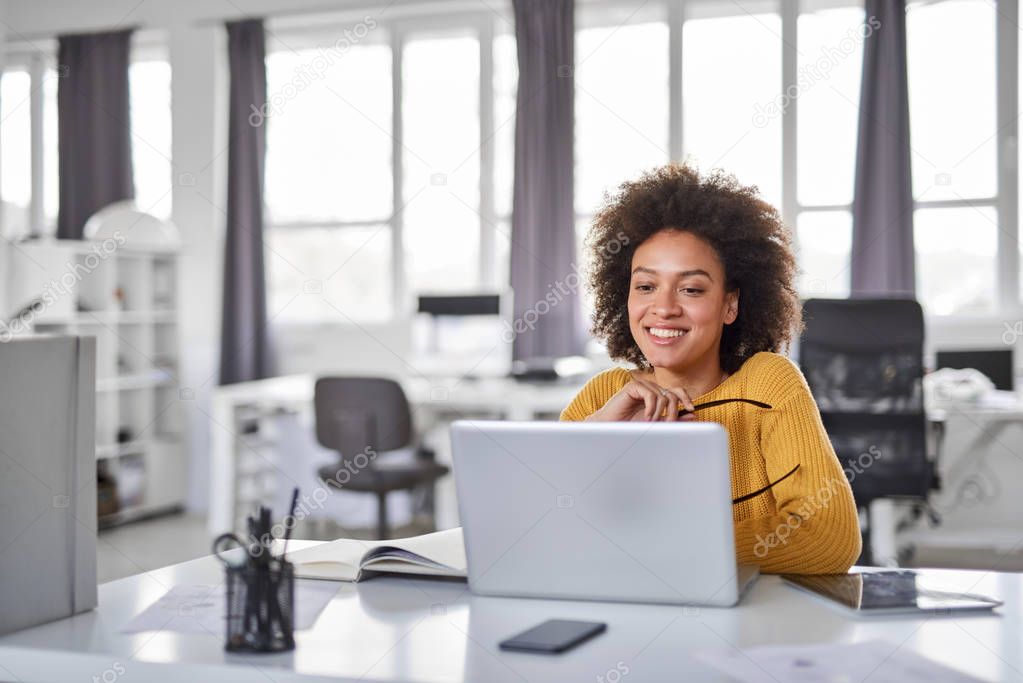Beautiful smiling mixed race businesswoman dressed casual sitting in office and using laptop.