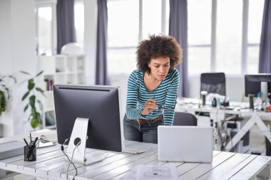 Güzel karışık ırk işadamı ofiste rahat ayakta giyinmiş ve bilgisayar monitörü bakarak.