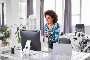 Güzel karışık ırk işadamı ofiste rahat ayakta giyinmiş ve bilgisayar monitörü bakarak.