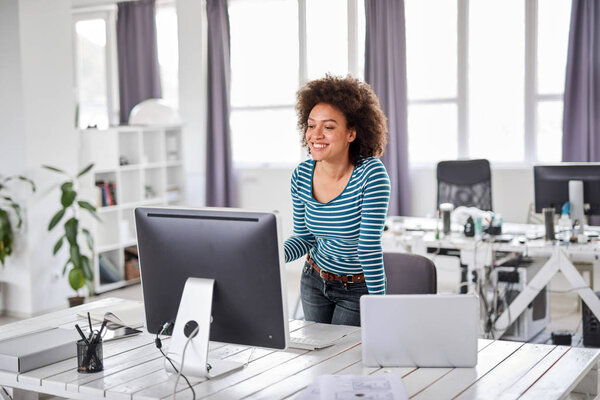 Красивая смешанная раса бизнесмен одет случайным стоя в офисе и глядя на монитор компьютера
.