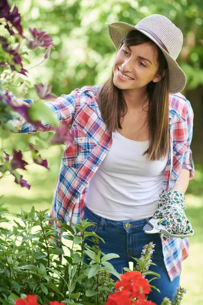 帽子、ガーデニング手袋と裏庭で彼女の花の世話をする作業服で美しい笑顔白人ブルネット. — ストック写真