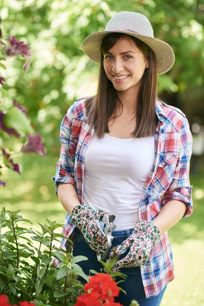 帽子、ガーデニング手袋と裏庭で彼女の花の世話をする作業服で美しい笑顔白人ブルネット. — ストック写真