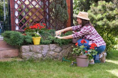 Şapka ve eldiven çömelme ve arka bahçesinde budama bitkileri ile çalışma giyim adanmış Kafkas esmer.