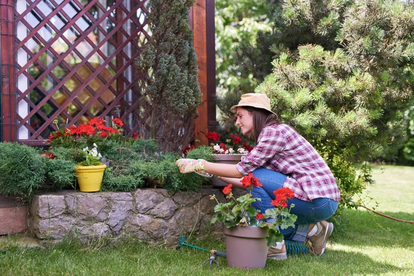 彼女の裏庭で帽子と手袋がしゃがみ、植物を剪定して、作業着で専用の白人ブルネット. — ストック写真