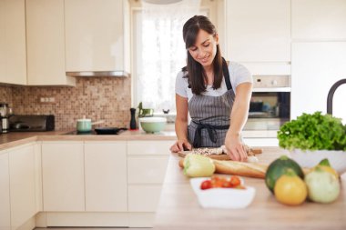 Güzel gülümseyen özel Kafkas esmer önlük mutfakta ayakta ve mantar doğrama. Masada bir sürü sebze var. Evde yemek pişirme konsepti.