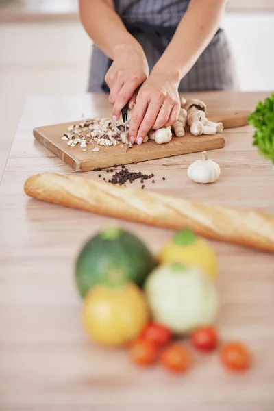 Toegewijde Kaukasische huisvrouw in schort staande in de keuken en het hakken van paddestoelen. Op tafel zijn veel groenten. Koken bij Home concept. — Stockfoto