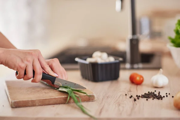 Вырезать изображение женщины, рубящей лук-порей на разделочной доске на кухне . — стоковое фото