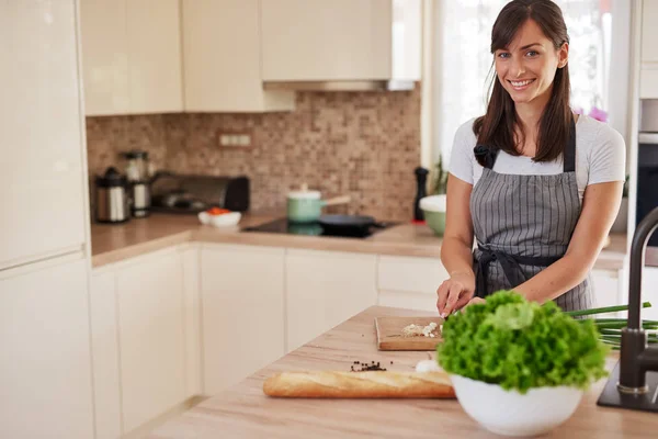 Leende kaukasiska kvinnlig i förkläde hugga purjolök i köket och förbereder middag. Beredning av inhemsk matkoncept. — Stockfoto