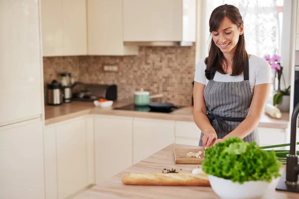 Glimlachend Kaukasische vrouwelijke chef-kok in schort hakken leek in de keuken en het voorbereiden van het diner. Bereiding van het huishoudelijk voedsel concept. — Stockfoto