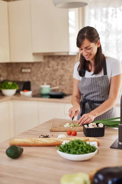 Smiling Caucasian female chef in apron chopping leek in kitchen and preparing dinner. Preparation of domestic food concept. — Stock Photo, Image