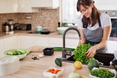 Mutfakta önlük yıkama salata neşeli çekici kafkas kadın. Evde akşam yemeği konsepti.
