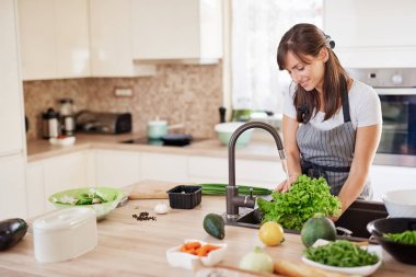 Mutfakta önlük yıkama salata neşeli çekici kafkas kadın. Evde akşam yemeği konsepti.