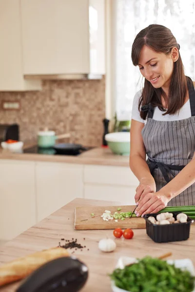 Chef feminino caucasiano sorridente em avental picando alho-porro na cozinha e preparando o jantar. Preparação do conceito de alimento doméstico . — Fotografia de Stock