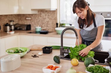 Mutfakta önlük yıkama salata neşeli çekici kafkas kadın. Evde akşam yemeği konsepti.