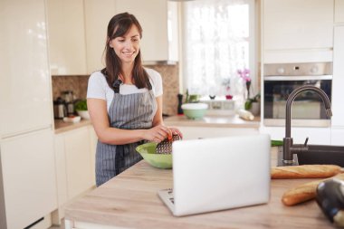 Genç Kafkas esmer önlük kase havuç rendeleme, akşam yemeği hazırlanıyor ve mutfakta dururken lapotp bakarak