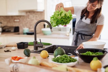 Mutfakta önlük yıkama salata neşeli çekici kafkas kadın. Evde akşam yemeği konsepti.