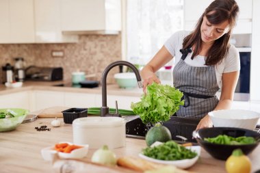 Mutfakta önlük yıkama salata neşeli çekici kafkas kadın. Evde akşam yemeği konsepti.