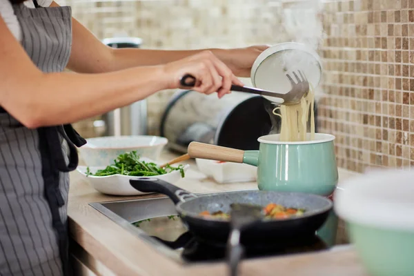 Mujer caucásica en delantal de pie junto a la estufa y preparando espaguetis. Preparación del concepto de comida italiana . — Foto de Stock