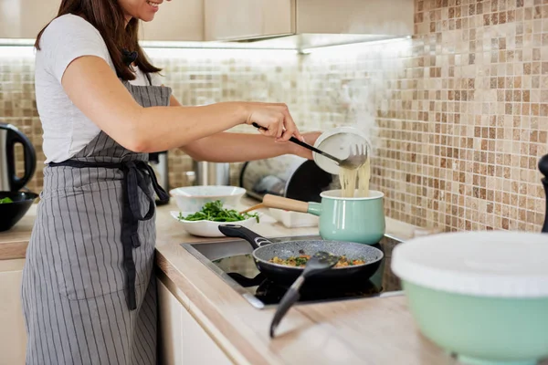 Белая женщина в фартуке стоит рядом с плитой и готовит спагетти. Подготовка концепции итальянской кухни . — стоковое фото