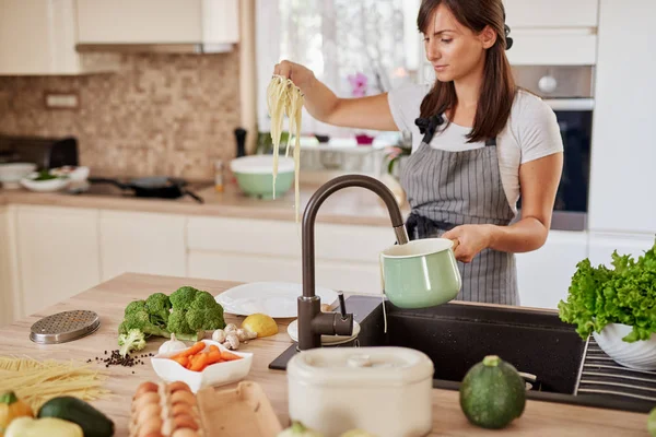 Mulher caucasiana de avental em pé na cozinha e colocando espaguete na placa. Preparação do conceito de alimento italiano . — Fotografia de Stock