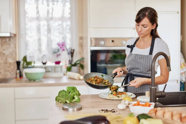Καυκάσια γυναίκα με ποδιά στέκεται στην κουζίνα και βάζει σάλτσα στα μακαρόνια. Προετοιμασία της ιδέας των ιταλικών τροφίμων. — Φωτογραφία Αρχείου