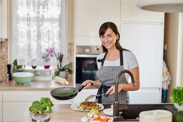 Kaukasisk kvinna i förkläde stående i köket och sätta sås på spaghetti. Beredning av italiensk matkoncept. — Stockfoto
