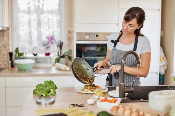 Mulher caucasiana de avental em pé na cozinha e colocando molho no espaguete. Preparação do conceito de comida italiana . — Fotografia de Stock