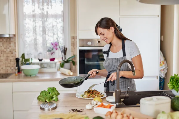 Mulher caucasiana de avental em pé na cozinha e colocando molho no espaguete. Preparação do conceito de comida italiana . — Fotografia de Stock