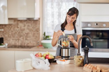 Mutfakta dururken blender sebze ve meyve koyarak önlük güzel Kafkas gülümseyen kadın.