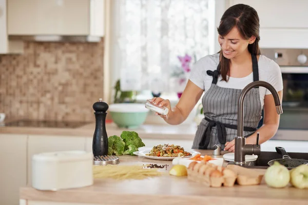 Morena branca bonito em avental de pé na cozinha e adicionando sal em massa deliciosa fresca. Preparação do conceito de alimento italiano . — Fotografia de Stock