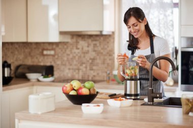 Güzel Kafkas gülümseyen kadın apron sebze koyarak güzel Kafkas gülümseyen kadın apron içinde sebze ve meyve blender koyarak mutfakta ayakta.