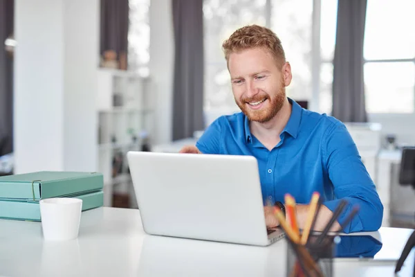 Unga kaukasiska anställd sitter på kontoret och skriver på laptop. Starta affärsidé. — Stockfoto