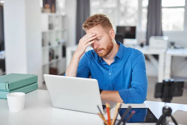 Νευρικός Καυκάσιος άνδρας εργαζόμενος έχει πονοκέφαλο ενώ κάθεται στο γραφείο. Κακή ημέρα στην εργασία έννοια. — Φωτογραφία Αρχείου