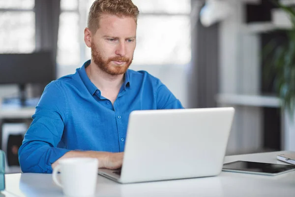 Joven empleado caucásico sentado en la oficina y escribiendo en el ordenador portátil. Concepto de creación de empresas . — Foto de Stock