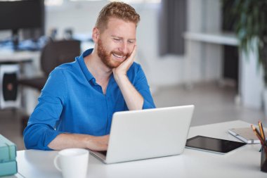 Genç gülümseyen çalışan ofiste oturan ve dizüstü bilgisayar kullanarak. İş konseptini başlatın.