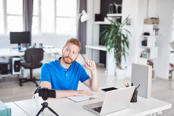 Hermoso empleado de jengibre caucásico vestido casual sentado en la oficina y pensando en la solución para el problema. Concepto de creación de empresas . — Foto de Stock