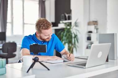 Kendini işine adamış çalışkan Kafkas çalışanı modern ofiste oturuyor ve not defterine bir şeyler yazıyor.