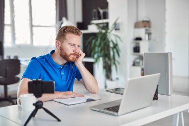 Yakışıklı Kafkas zencefil çalışan rahat dizüstü bilgisayar bakarak giyinmiş ve modern ofiste otururken büyük proje üzerinde çalışıyor.