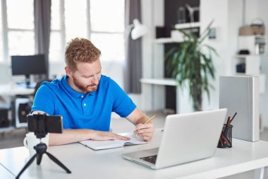 Kendini işine adamış çalışkan Kafkas çalışanı modern ofiste oturuyor ve not defterine bir şeyler yazıyor.