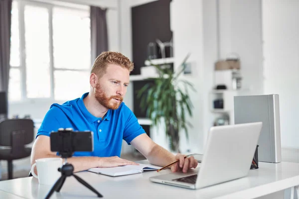 Guapo caucásico jengibre empleado vestido casual mirando portátil y trabajando en gran proyecto mientras está sentado en la oficina moderna . — Foto de Stock