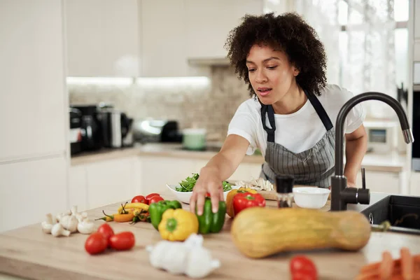 Vacker blandad ras hemmafru når för grön peppar när du står i köket. Middag förberedelse. B. — Stockfoto