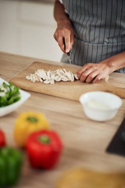 Mutfakta ayakta ve mantar doğranan önlük karışık ırk kadın yakın çekim.