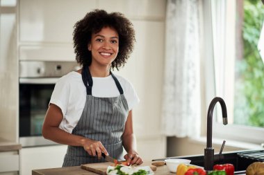 Önlüklü, havuç kesen ve mutfakta yemek hazırlayan çekici melez bir kadın. Mutfak tezgahında sebze var..
